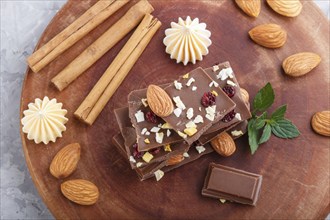 A pieces of milk chocolate with almonds and dried fruits on a brown wooden board on a gray concrete