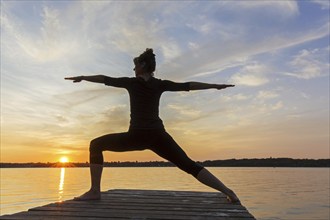 Woman practicing yoga posture Virabhadrasana II, Warrior Pose, lunging standing asana on jetty at