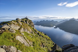 Climber on the summit of Dronningsvarden or Stortinden, behind sea and fjord Umvågsundet,