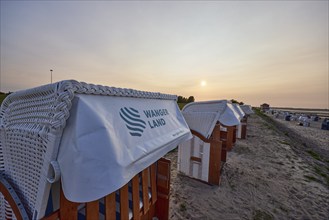 Beach chair with the inscription Wangerland in the backlight of the sunset on the beach of the