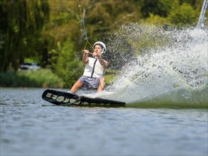 Young man with wakeboard in lake, water sports, water skiing in wakepark