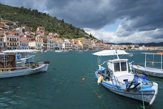 Harbour town with boats in the foreground and a forested range of hills in the background under a