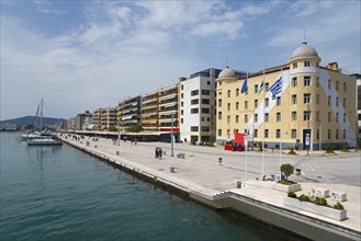 Harbour promenade next to calm water with sailing boat and people along the picturesque buildings,