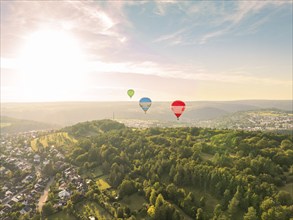 View of several hot air balloons over a wooded landscape at sunset near a town, Calw, Black Forest,