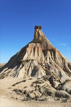 Steep rock formation in a dry desert landscape under a clear blue sky, Castildetierra, Bardenas