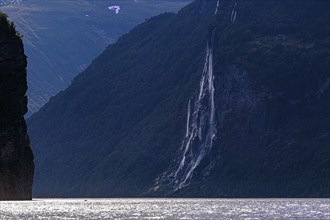 The Seven Sisters waterfall cascades along a steep cliff face into the Gairangerfjord, surrounded