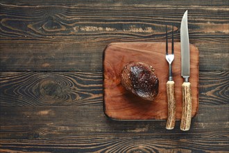 A beautifully grilled steak rests on a rustic wooden cutting board, accompanied by a knife and fork