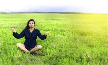 Relaxed woman doing yoga in the field. Woman meditating in the field