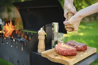 A close-up view of hands using a wooden hand mill to season beef steak with pepper