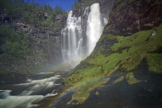 Picturesque waterfall cascading over rocks into a river, surrounded by lush greenery and forest in