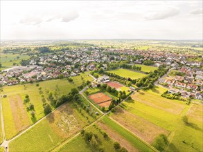 Panoramic view of a town with many houses, surrounded by green fields and under a cloudy sky,