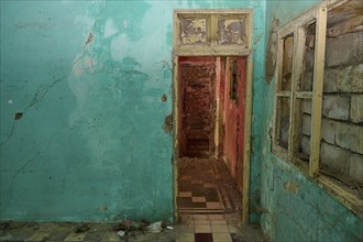 Ruined room with bright blue wall colour and destroyed door, window and a badly damaged floor,