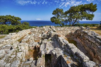 Ancient ruins with stone walls and views of the sea and trees under a blue sky, Kamiros,