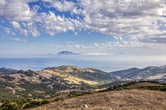 Wide landscape with mountains and sea, blue sky with clouds, near Tarifa, view to Morocco