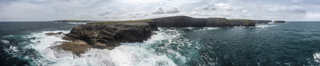 Panorama of the coastline with rugged cliffs and undulating ocean under a cloudy sky, Kilkee