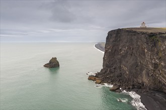 Steep cliff on the coast with a lighthouse under a grey sky, Dyrhólafjara, Dyrhólaey or Dyrholaey,