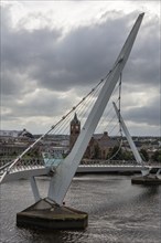 Modern bridge against a cloudy sky with a tower in the background, Londonderry