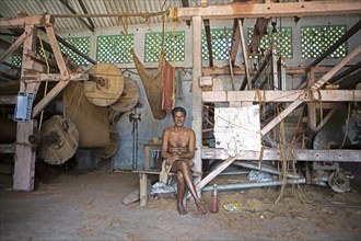 Indian worker, 68 years old, sitting in the weaving mill of the Labourers Coir Mats and Mattings