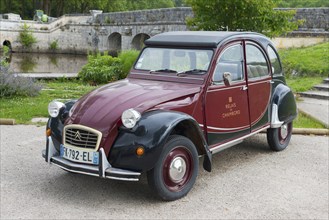 Retro Citroën 2CV vintage car in red and black, parked on a road in front of a stone bridge in a