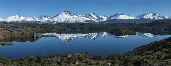 The snow-covered Mt. Cerro Castillo is reflected in a lake, small farm by the lake, Panorama,