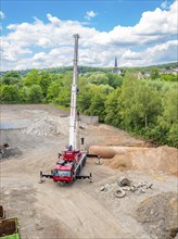 A construction site with a crane and pile of gravel, surrounded by vegetation, sky, clouds and