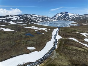 Melting ice on mountain lake Bessvatn, Mt. Besshö, river Bessa, old snow in early spring, aerial