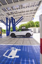 White electric car parked under a modern solar charging station, surrounded by nature, ENBW