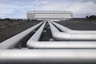 Geothermal power plant Steam pipe running to metallic building under grey sky. Technical, modern