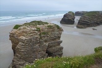 Huge rocks on the beach overlooking the sea. People walking along the shore under a cloudy sky,