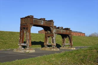 Rusty metal structures on an abandoned industrial site with a green meadow and blue sky, Ilseder