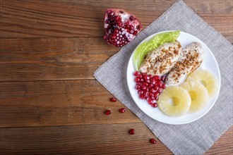 Fried chicken fillets with lettuce, pineapple and pomegranate seeds on brown wooden background,