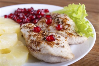 Fried chicken fillets with lettuce, pineapple and pomegranate seeds on brown wooden background,