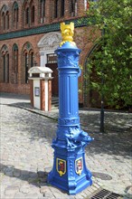 A traditional, blue-painted hydrant on a cobblestone path next to a brick building, water point,