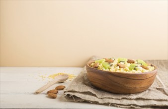 Millet porridge with kiwi and almonds in wooden bowl on a white and orange background and linen