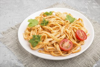 Semolina pasta with tomato pesto sauce, orange and herbs on a white ceramic plate on a gray