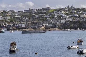 Sailing ship and boats on the water with a coastal town in the background, Fowey Landing, Cornwall,