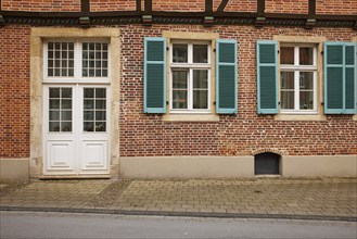 White entrance door and windows with blue-green shutters on a brick house in Warendorf, Warendorf