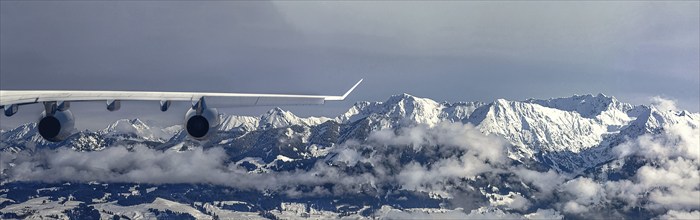 An aeroplane flies over a snow-covered mountain landscape and misty forests, the sky is cloudy