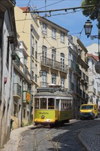 A yellow-green tram winds its way along a narrow, steep alley surrounded by old buildings, Tram,