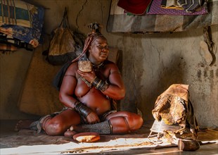 Traditional Himba woman caring for her body with smoke, interior of the first woman's mud hut in a