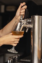 Close-up of a female bartender's hand on a beer tap, pouring a fresh beer in a lively bar setting.