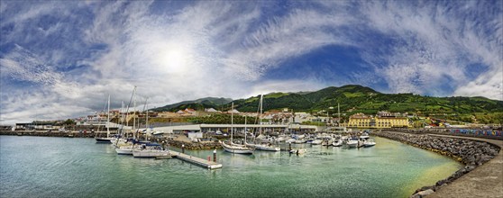 A picturesque harbour with yachts and boats, surrounded by buildings, mountains and a cloudy sky