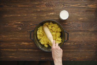 Hand of woman holds wooden potato masher and making mashed potatoes, top view