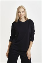 A woman with long blonde hair stands confidently, wearing a simple black outfit. She embraces a