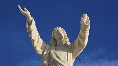 Close-up of a statue of Jesus with outstretched arms in front of a clear blue sky, Agios Nikolaos