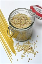 Fregola in wooden spoon and glass container with spaghetti, pasta variety from Sardinia, Italy,