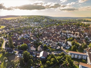 Aerial view of a dense cityscape with houses, streets and trees surrounded by hills and clouds,