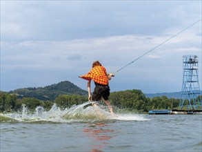 Man with red hair and flapping shirt on wakeboard, water ski and wakepark, Stráž pod Ralskem, Czech