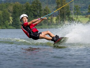 Boy or girl, happy summer holiday with wakeboard, water splashes, red life jacket, water skiing and