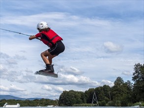 Boy or girl jumping and flying with wakeboard, water sports and water skiing in the wakepark, Stráž